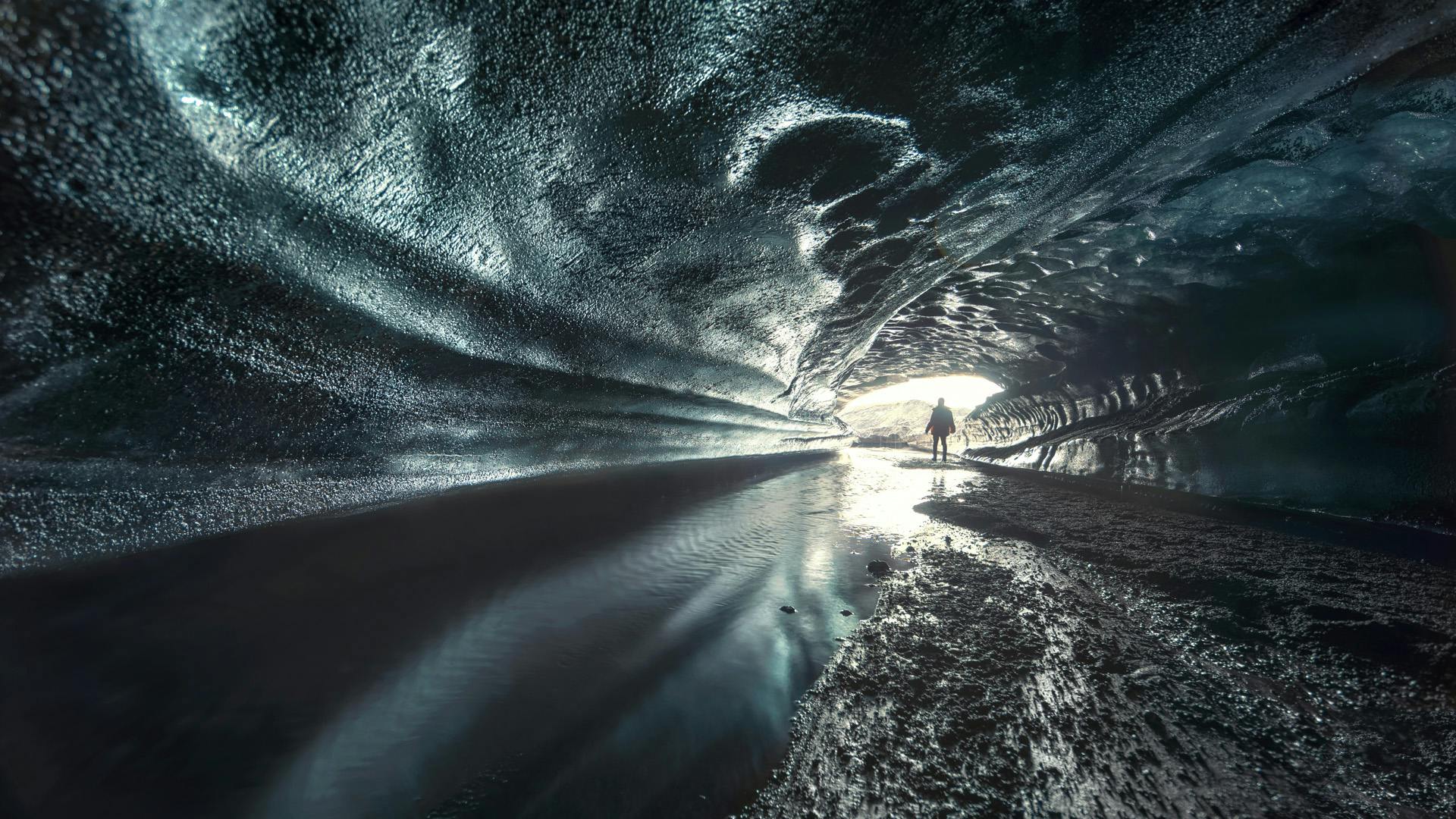 Silhouette of a person standing in front of an ice cave entrance.