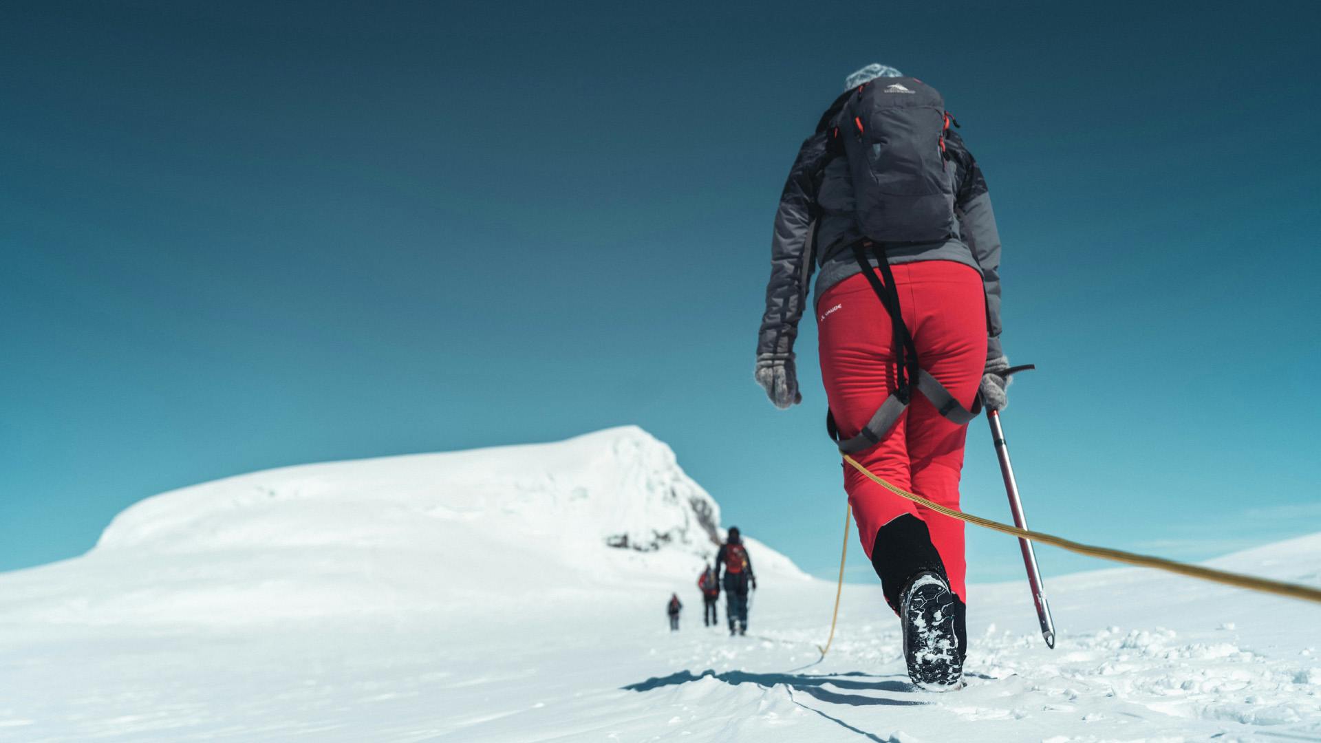 Group of people walking on snow towards the mountain.