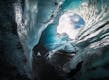 Person looking up to a hole that is situated on the ceiling of an ice cave.