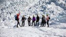 A group of people with their tour leader hiking on a glacier.