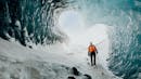 A person using an orange jacket is standing and looking at the ceiling of an ice cave.
