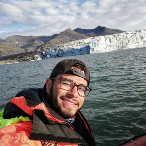 A man smiling at the camera and paddling on a glacier lagoon.
