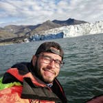 A man smiling at the camera and paddling on a glacier lagoon.