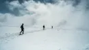 Three person walking on top of a mountain covered with snow.