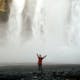 Happy woman with arms in the air photographed with a waterfall behind her.