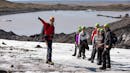 A glacier guide points towards the top of the glacier while the group is looking at it.