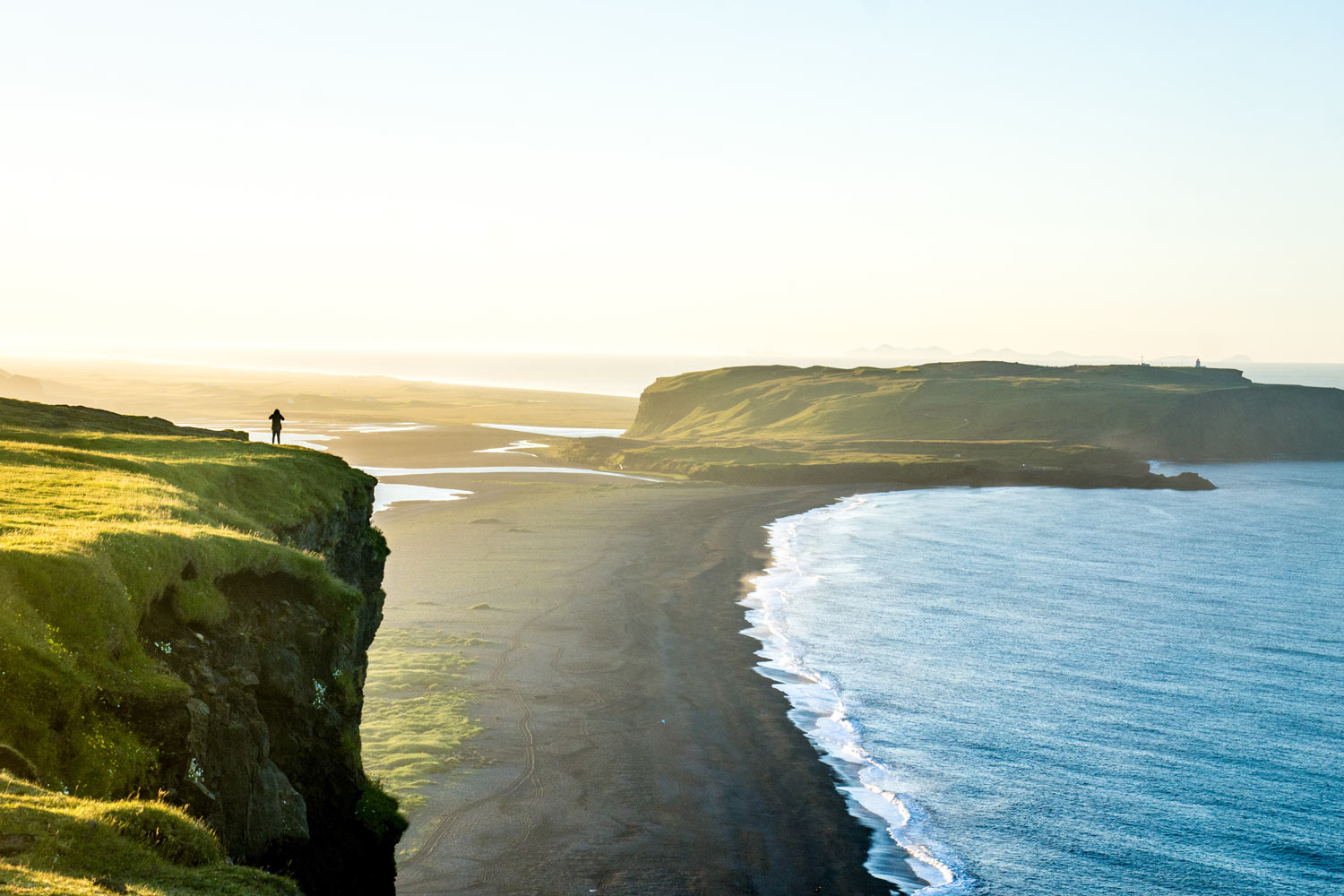 Person standing near a cliff while photographing the landscape during summer time.
