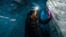 Woman using a flash light on a helmet, touching the ice inside an ice cave.