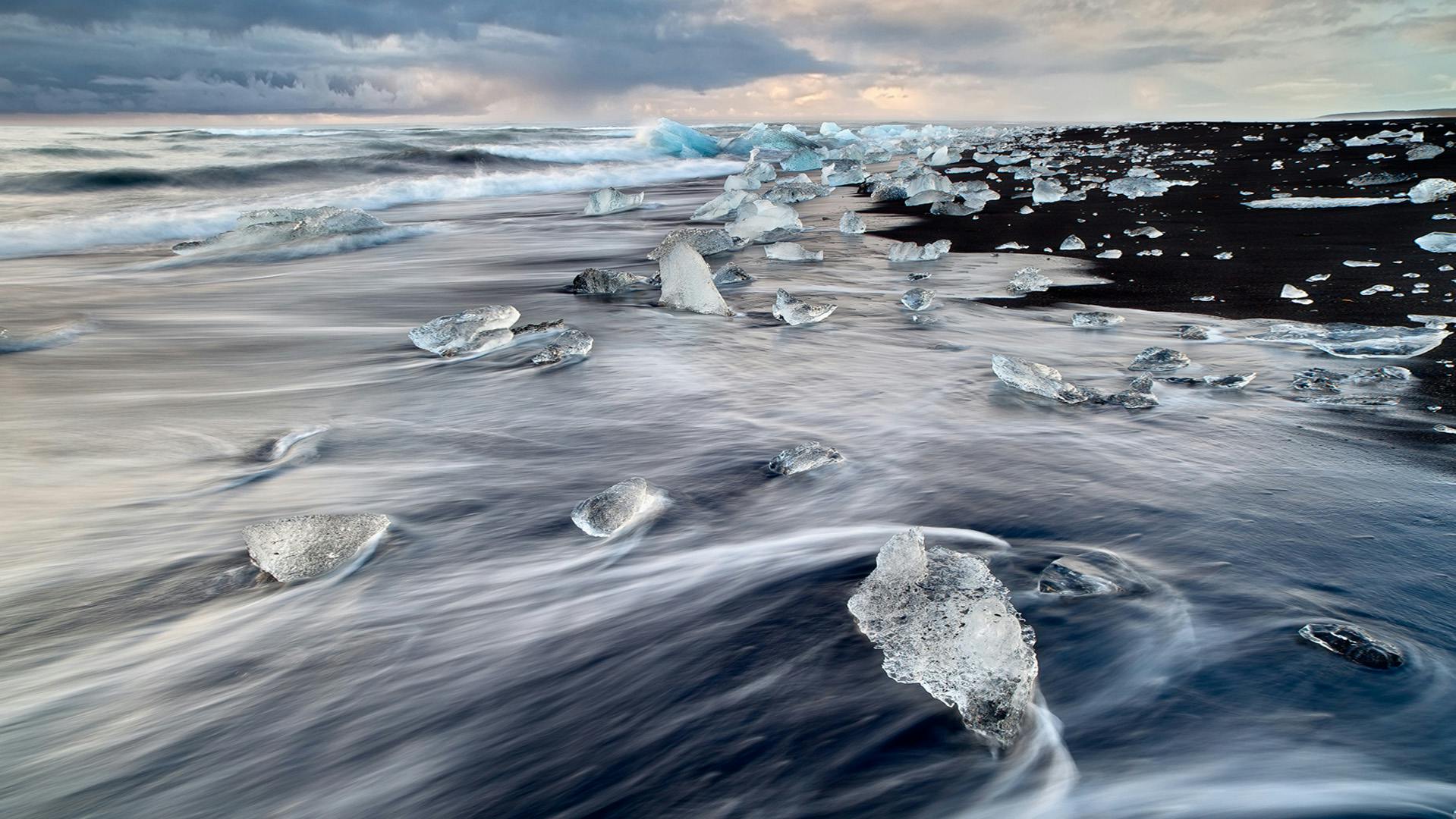 Black sand beach with chunks of ice trapped on the sand.
