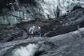 Two people walking on top of a glacier covered with ashes.
