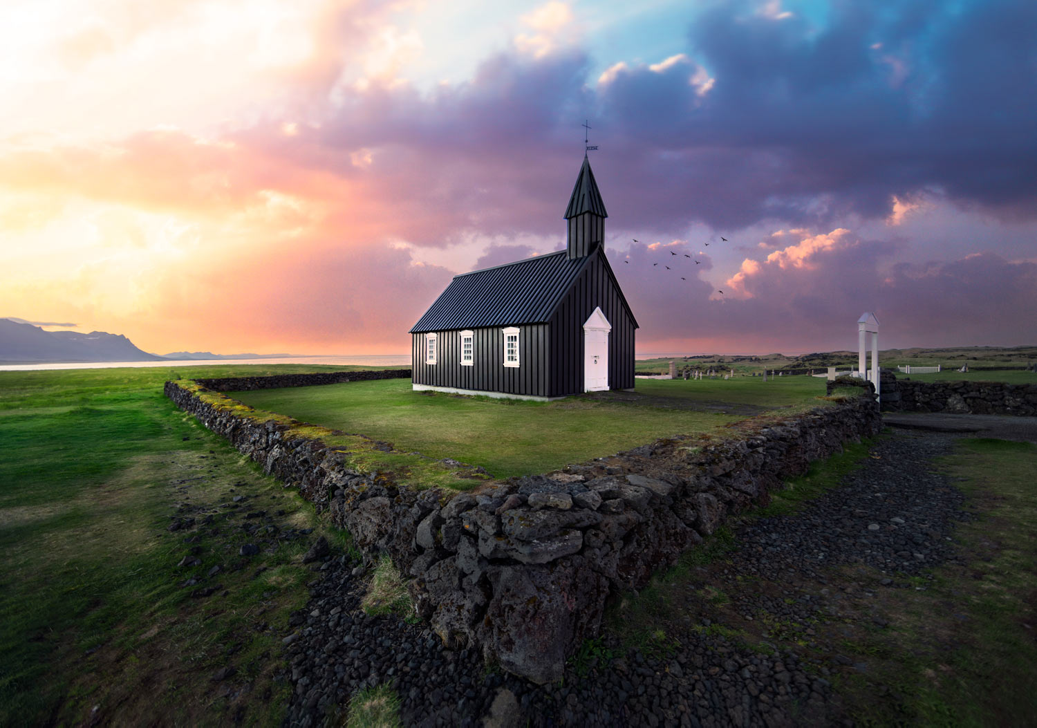 Small stone walls with a black church inside the perimeter, a colorful sunset is striking in background.
