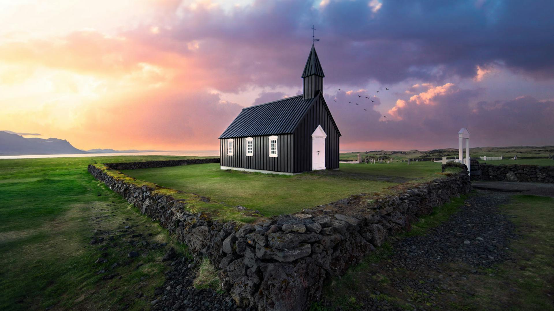 Small stone walls with a black church inside the perimeter, a colorful sunset is striking in background.