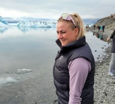 A blonde girl with glasses standing next to glacier lagoon