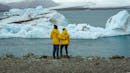 A couple in yellow hugging each other while watching big chunks of ice floating on a glacier lagoon.