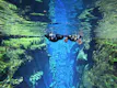 Two people snorkeling on translucent glacial water between a tectonic fissure.