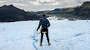 A man holding his helmet and looking to the horizon, where there is a glacier lagoon.
